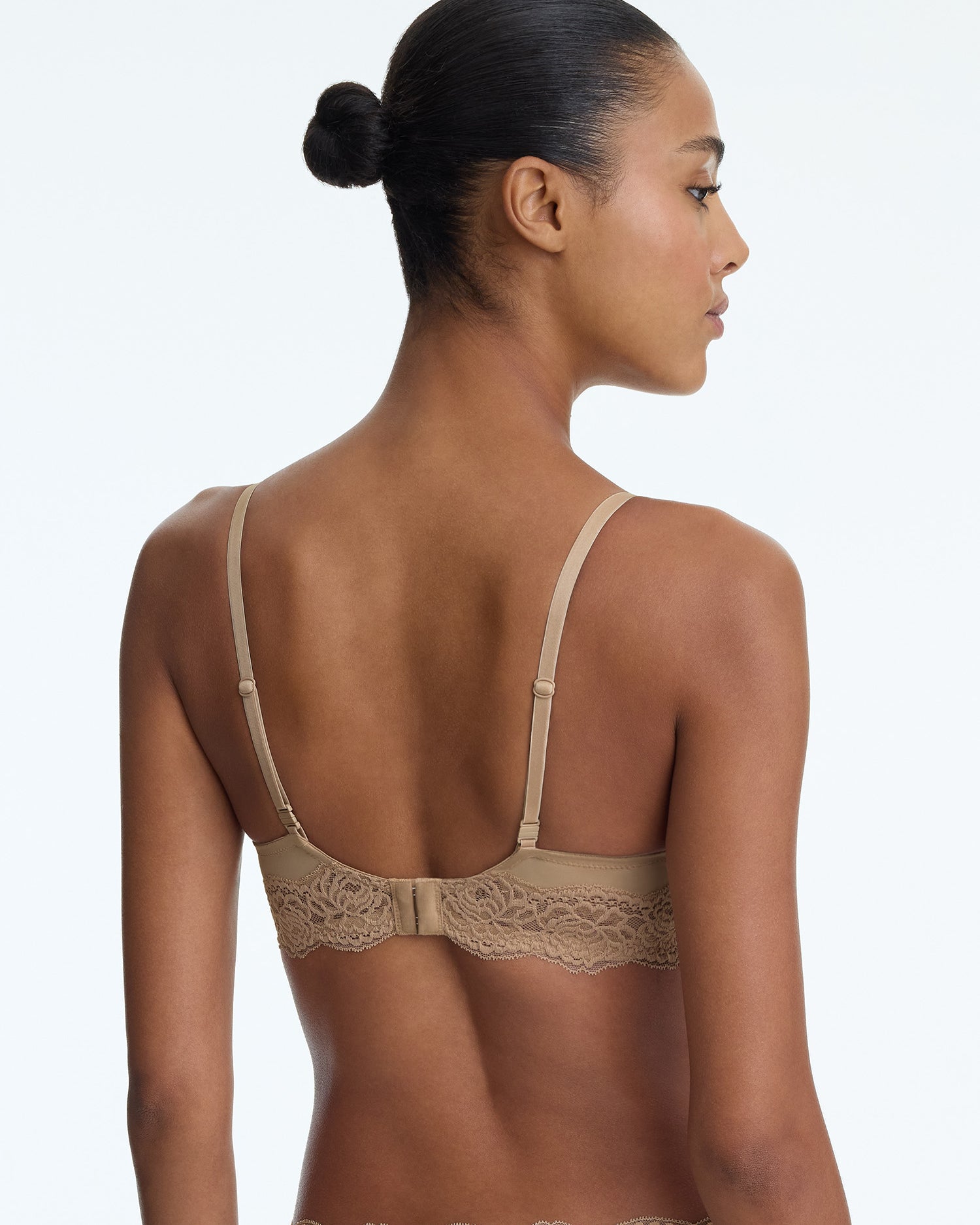 Woman wearing a beige bralette with lace details on a plain background