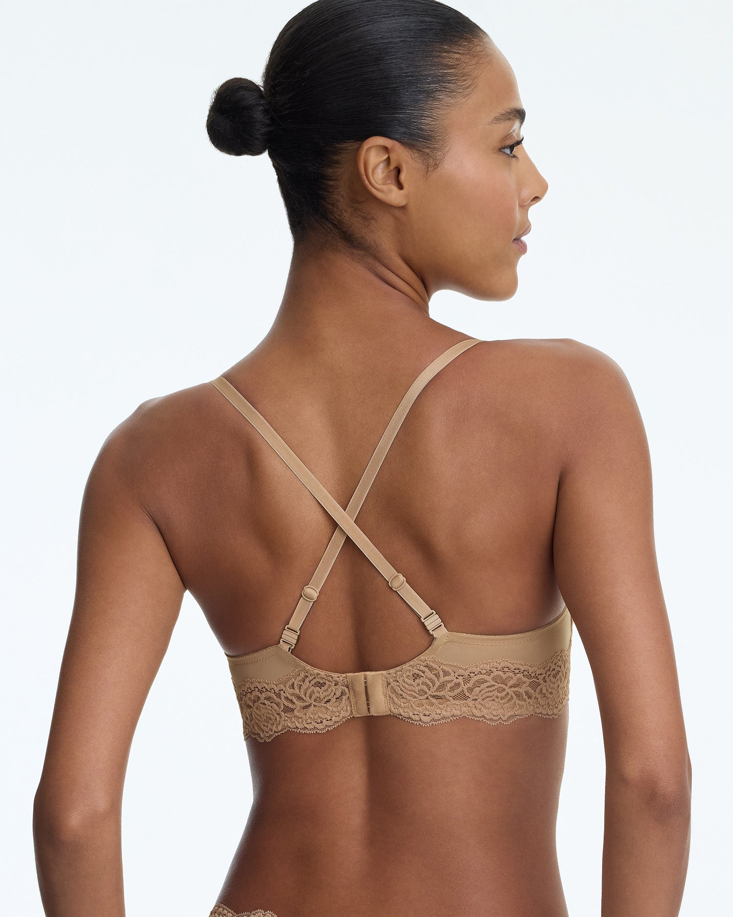 Woman wearing a beige bra with lace details on a plain background