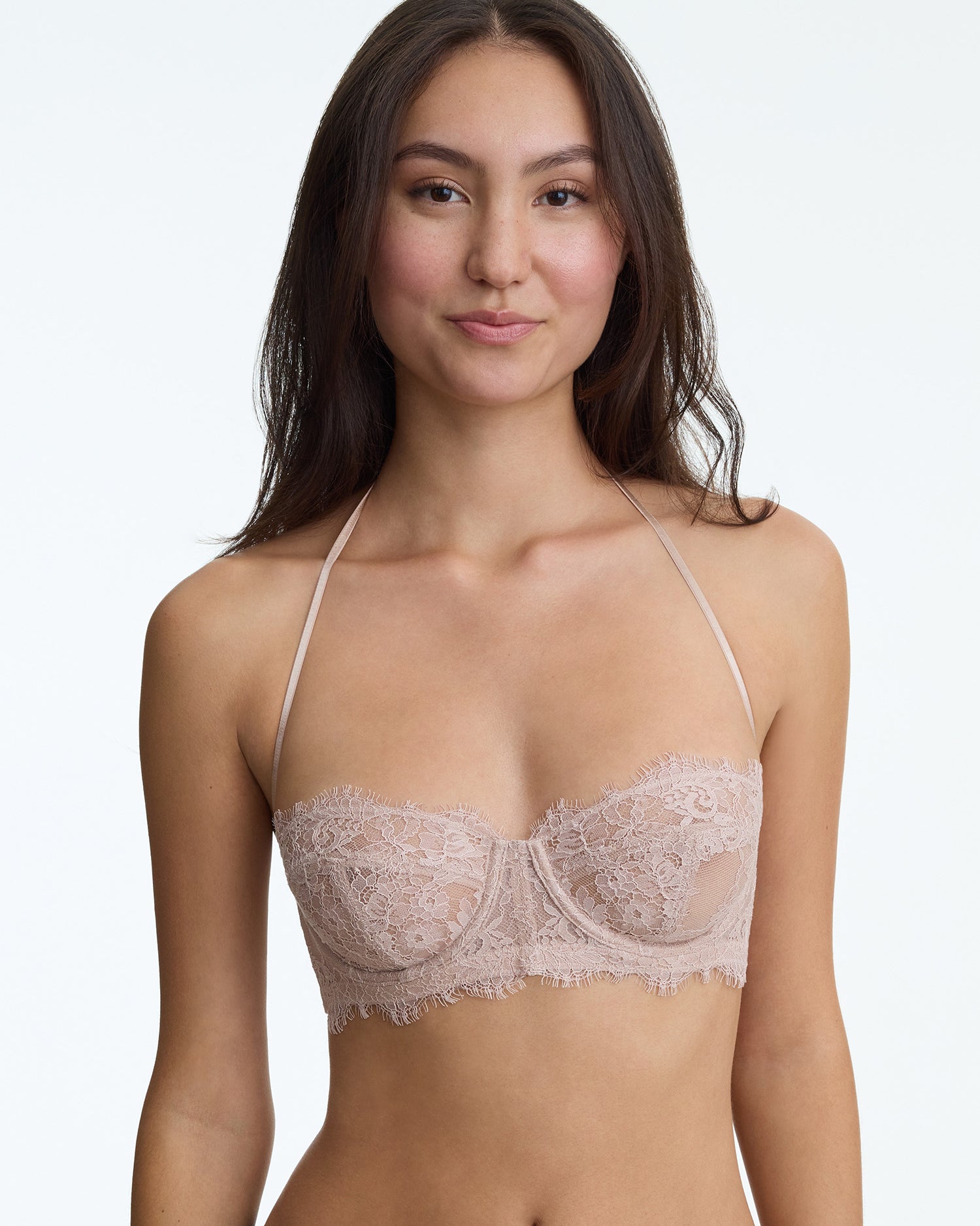 Woman wearing a beige lace bralette against a plain background
