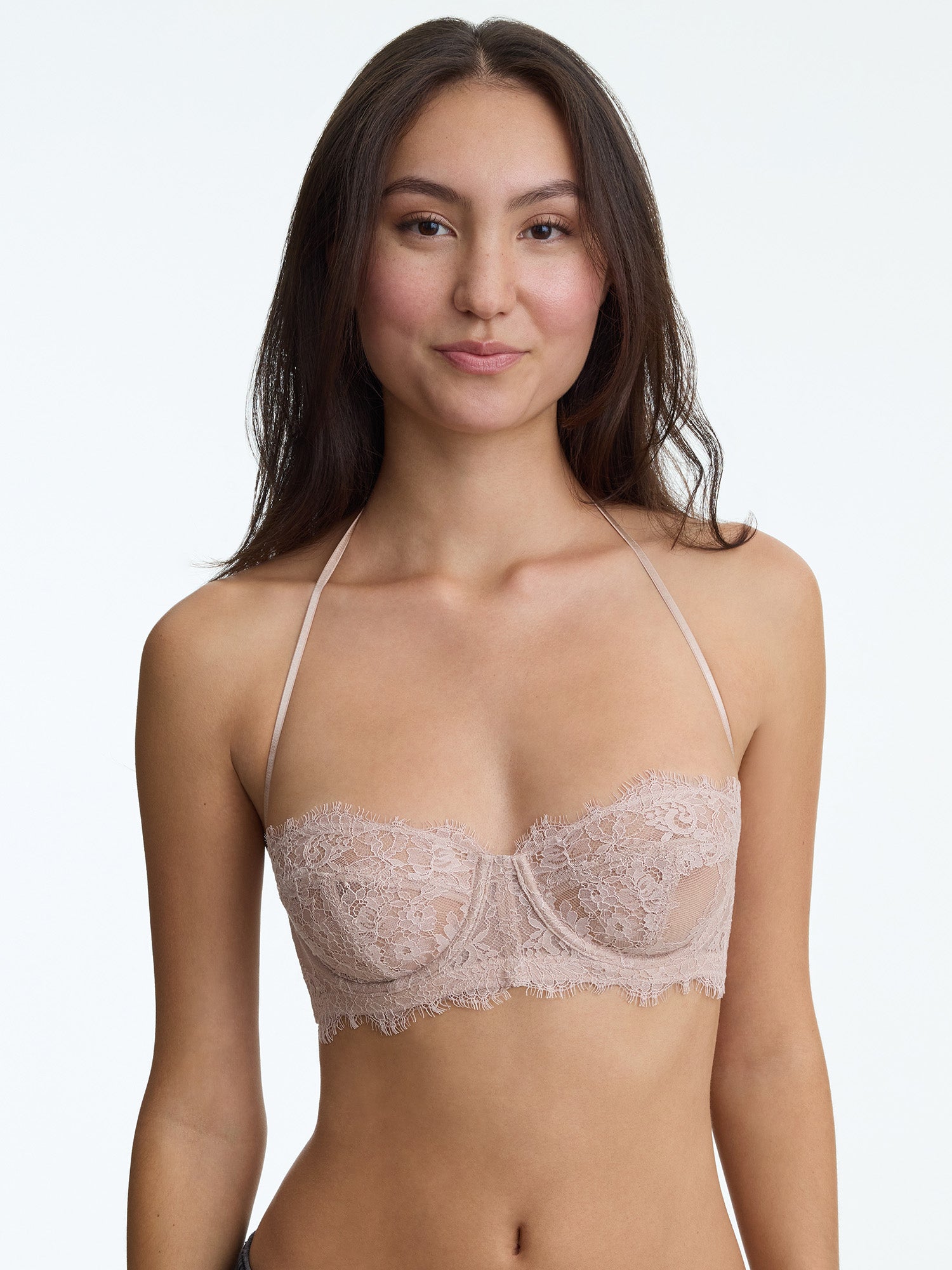 Woman wearing a beige lace bralette against a plain background