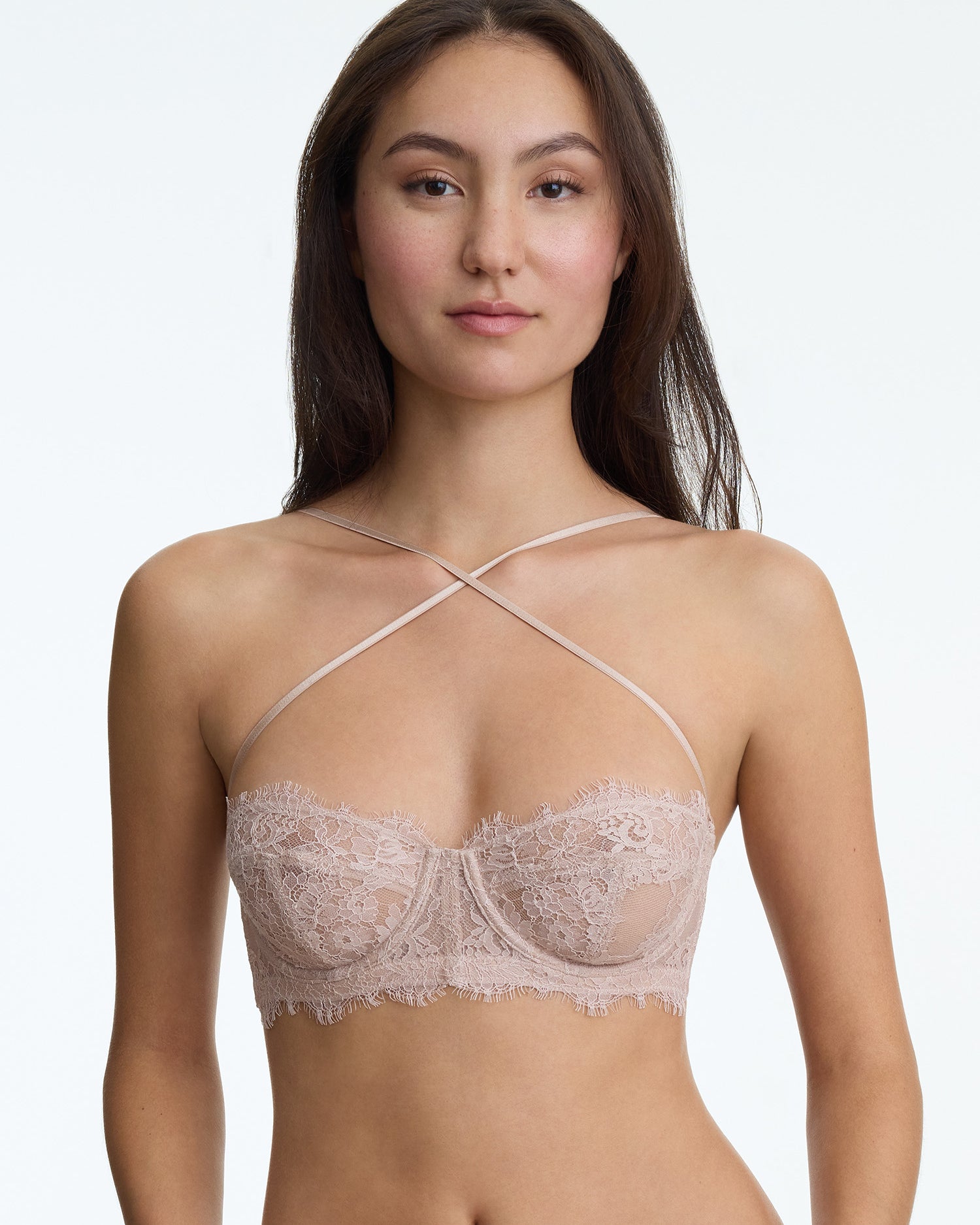 Woman wearing a beige lace bra against a plain background