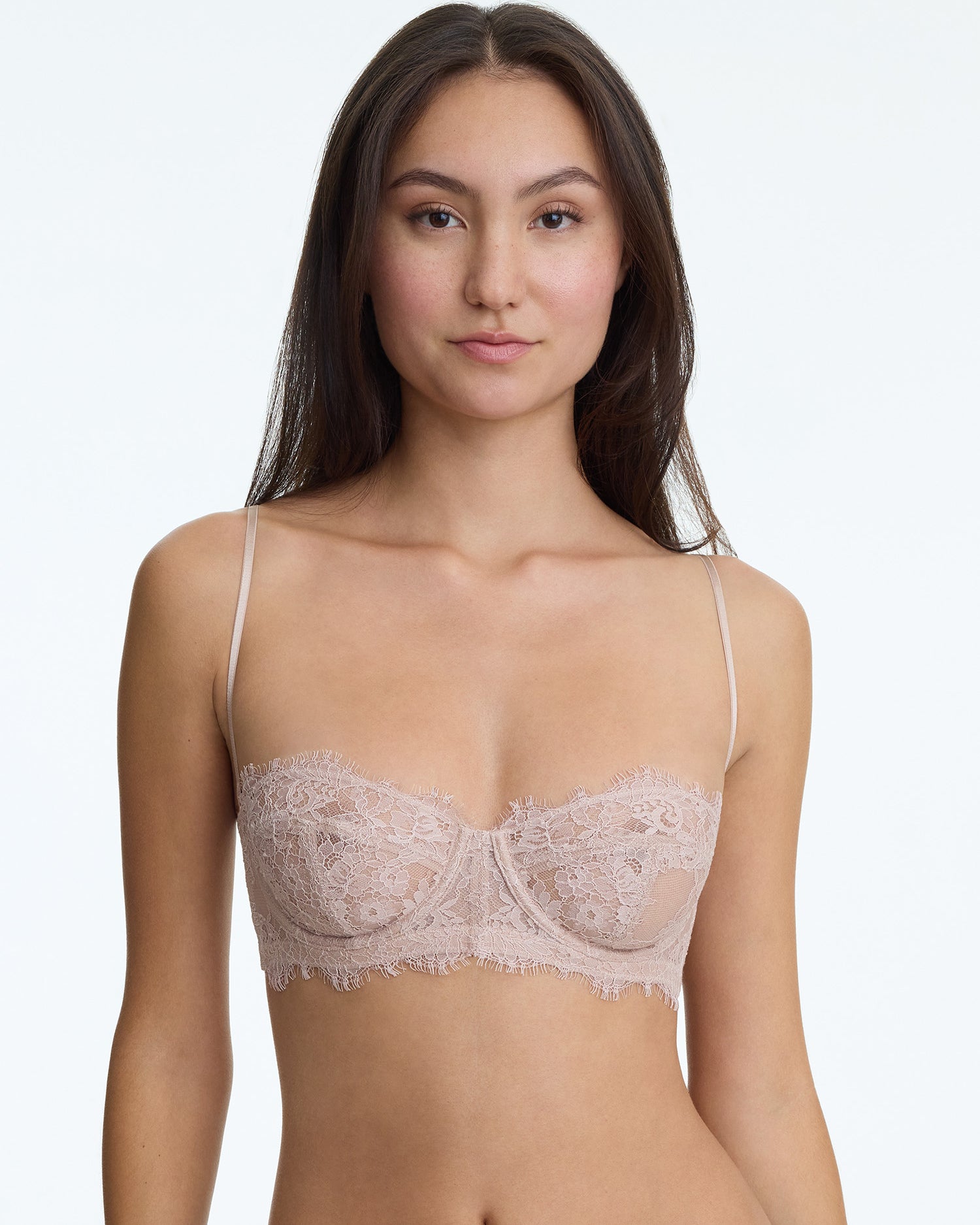 Woman wearing a beige lace bra against a plain background