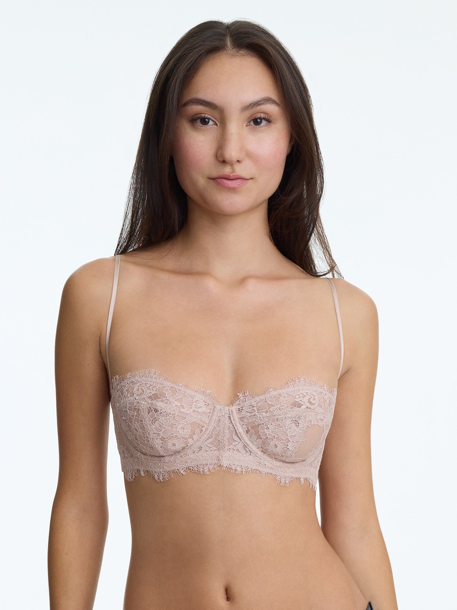 Woman wearing a beige lace bra against a plain background