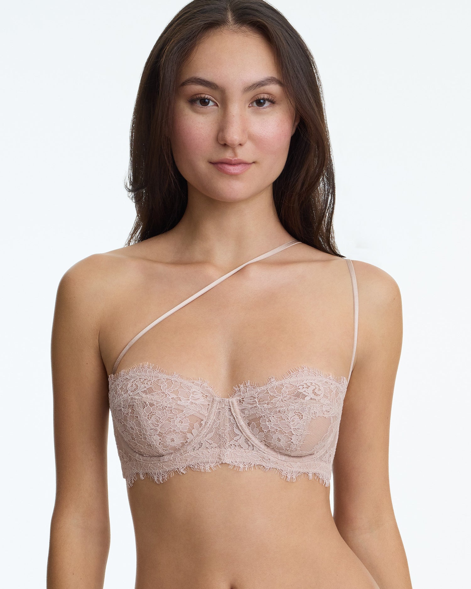 Woman wearing a beige lace bra against a plain background