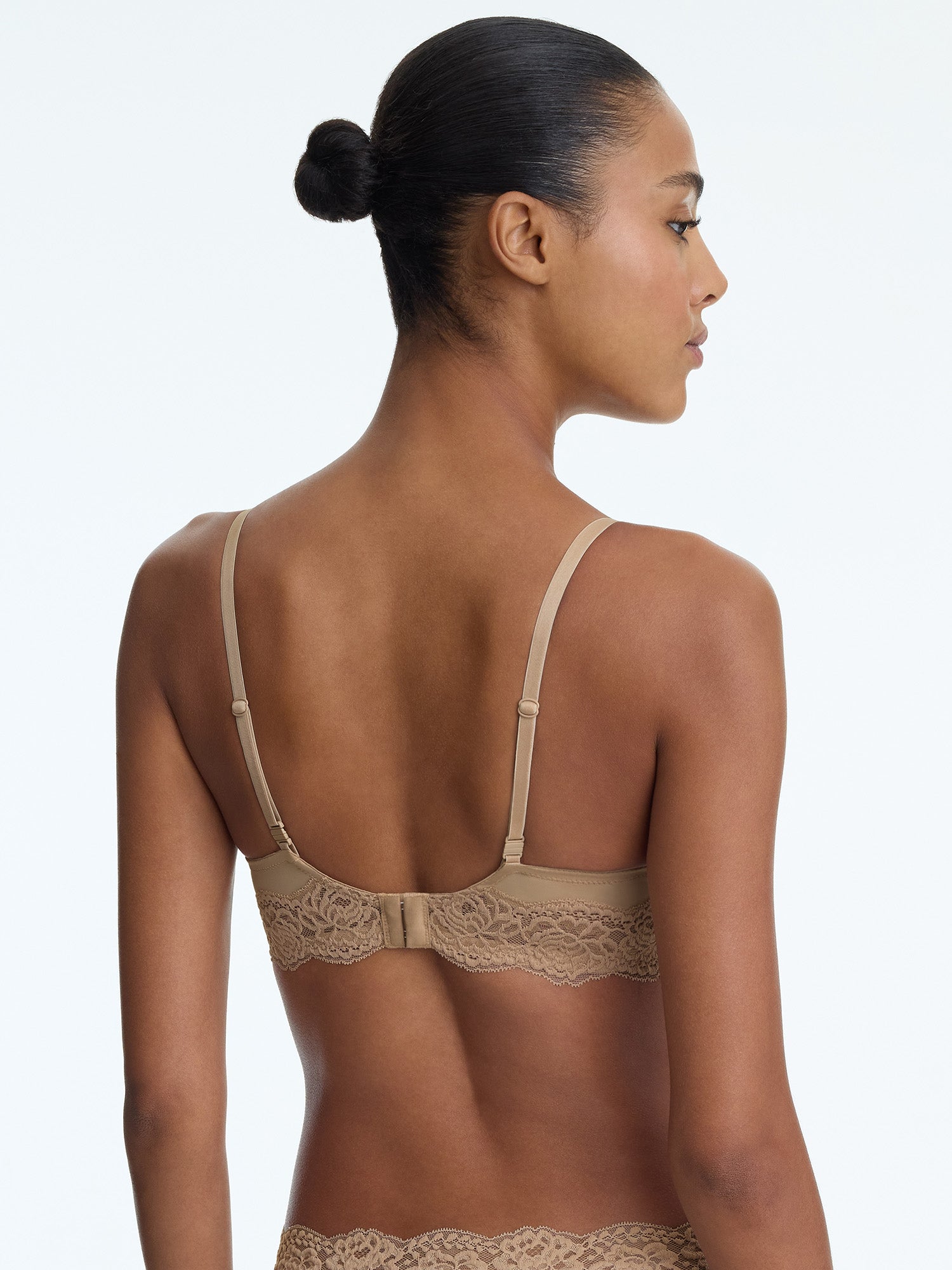 Woman wearing a beige bralette with lace details on a plain background