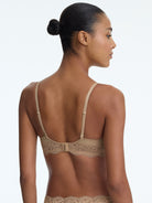 Woman wearing a beige bralette with lace details on a plain background