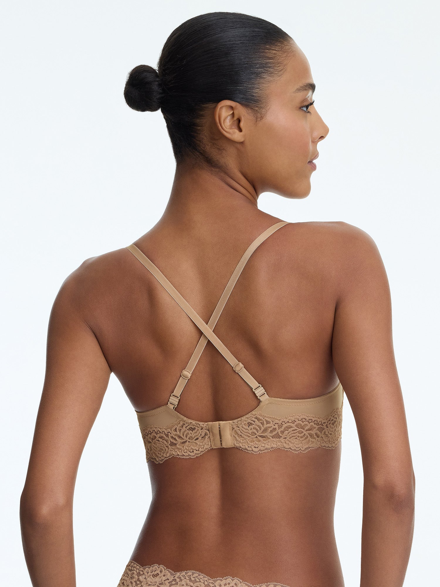 Woman wearing a beige bra with lace details on a plain background