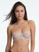 Woman wearing a beige lace bralette against a plain background