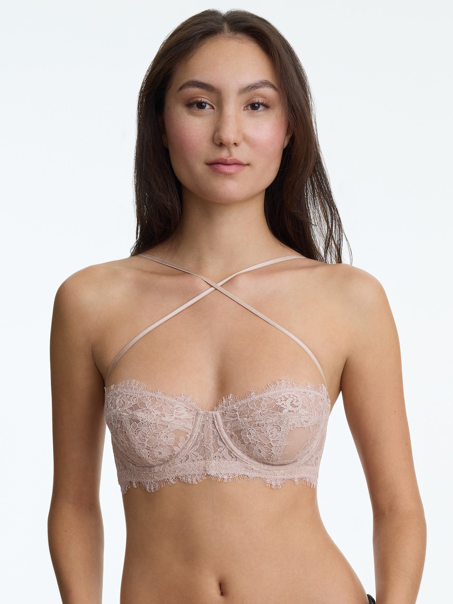 Woman wearing a beige lace bra against a plain background