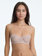 Woman wearing a beige lace bra against a plain background
