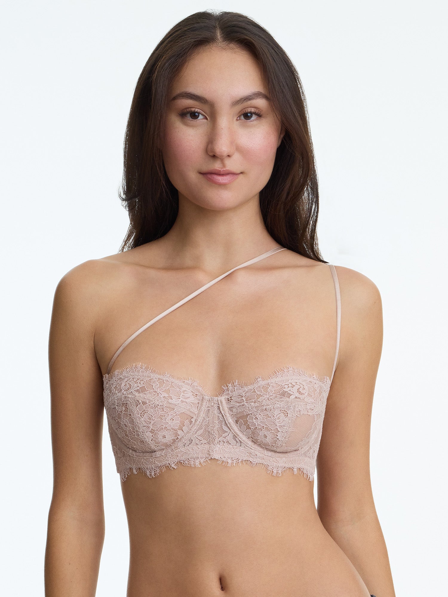 Woman wearing a beige lace bra against a plain background