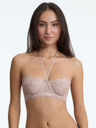 Woman wearing a beige lace bralette against a plain background